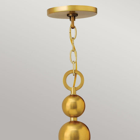 A close-up of a modern gold pendant light fixture with a linked chain and spherical design evokes mid-century aesthetics. This fixture, akin to the Zelda 8 Light Chandelier in Vintage Brass, is suspended from a circular ceiling mount against a neutral backdrop.