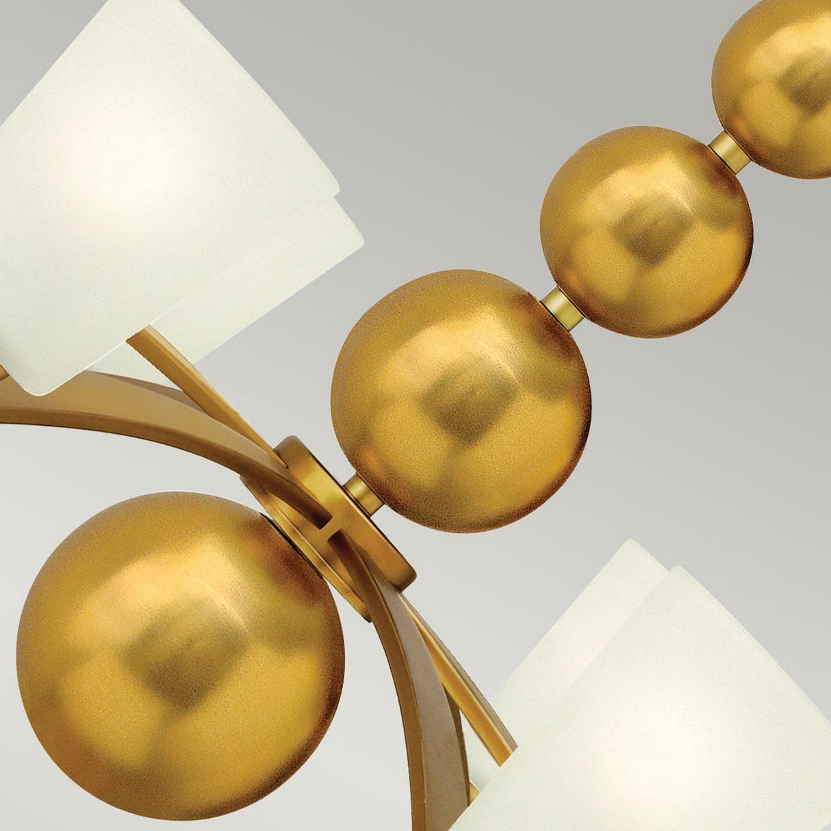 A detailed view of a mid-century design features golden spheres arranged in decreasing size, similar to the Zelda 8 Light Chandelier - Vintage Brass. These spheres sit on a vintage brass frame, with each end featuring white, square-shaped lampshades. The background displays a gentle gradient.