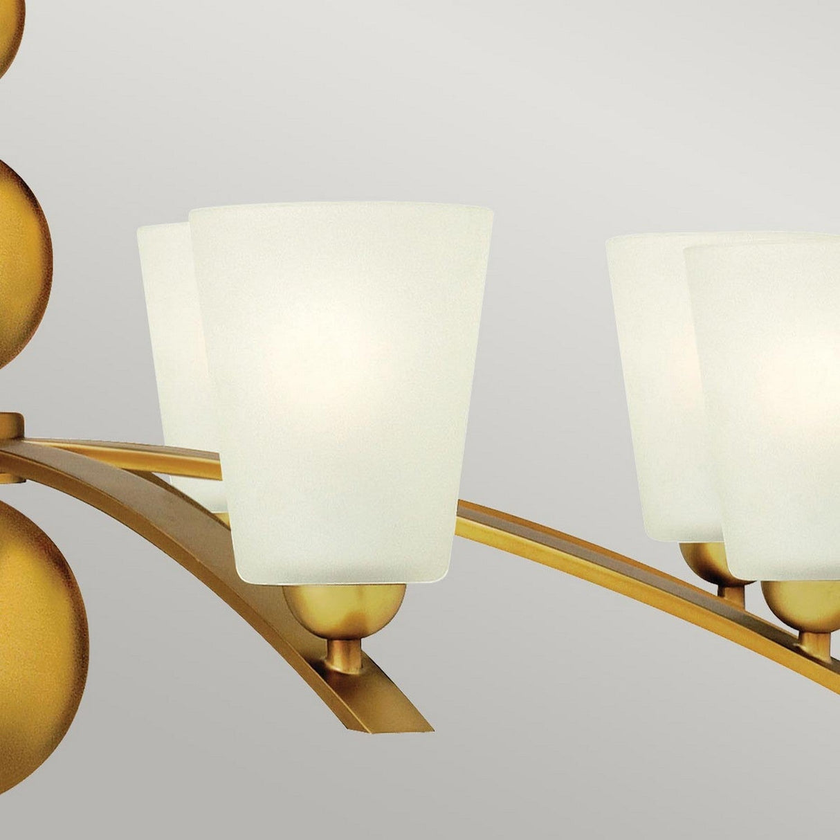 This close-up highlights the Zelda 8 Light Chandelier - Vintage Brass, blending mid-century style with modern sophistication. Its frosted glass shades rest on a sleek curved golden frame, creating a chic and contemporary atmosphere while emitting a gentle ambient glow.
