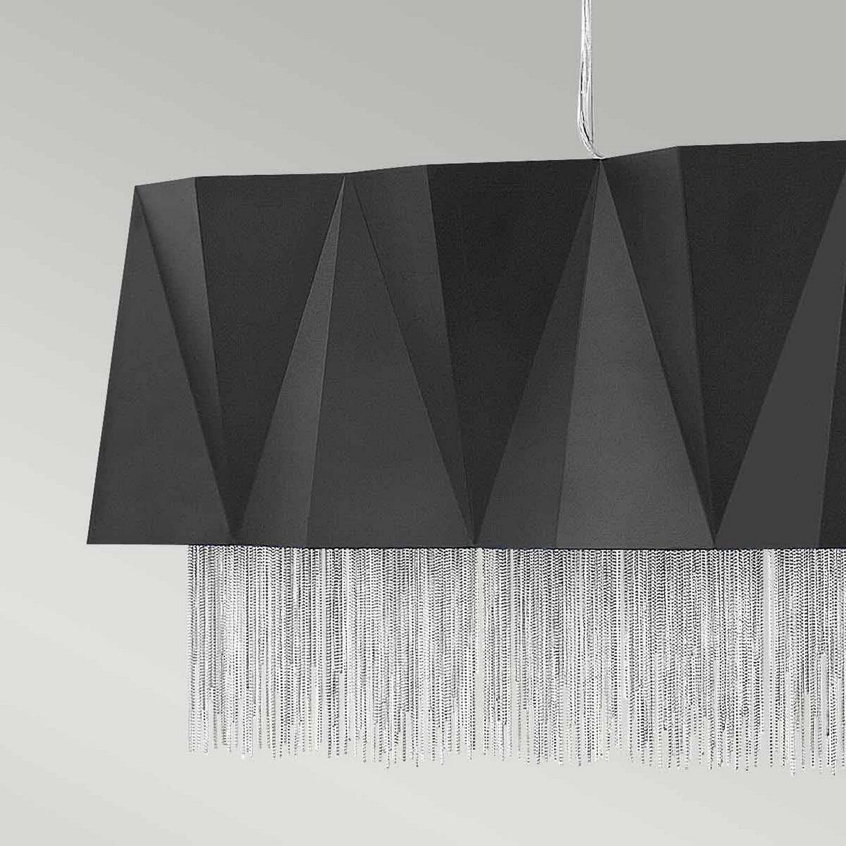 The Zuma 6 Light Linear Chandelier, featuring a sleek satin black and silver geometric shade adorned with a silver chain fringe, provides ample lighting for contemporary spaces. It's the perfect choice for modern interiors, exuding elegance against a light gray background.