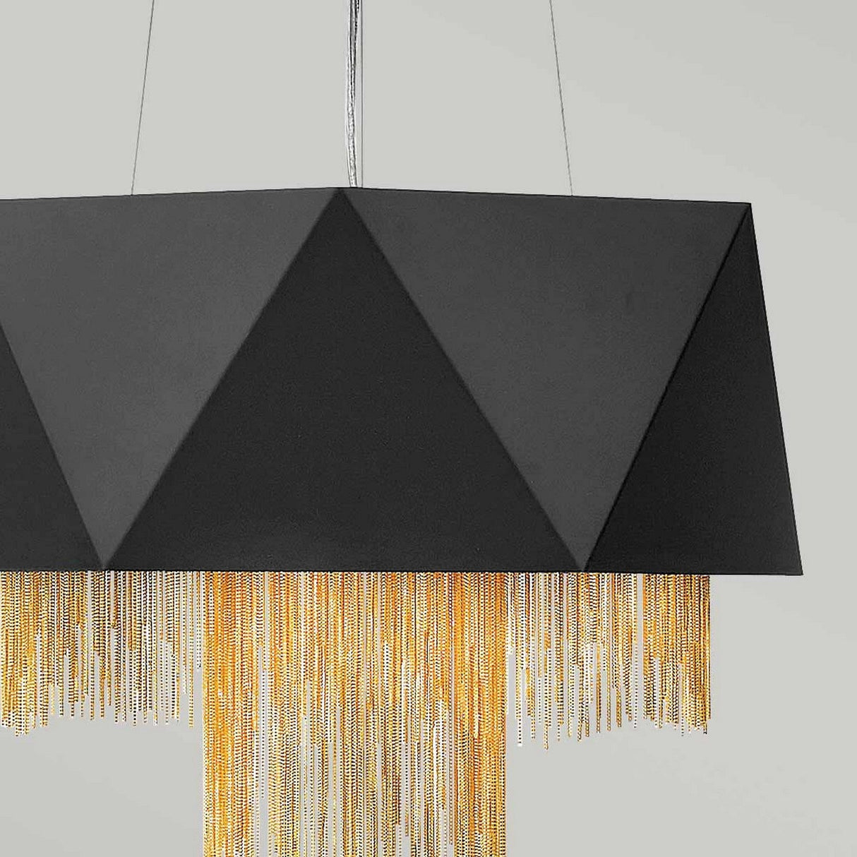 The Zuma 6 Light Chandelier in Satin Black and Gold features a geometric pendant design with a triangular faceted structure that hangs elegantly from the ceiling. It includes gold chain fringe draping from the bottom, bringing a touch of contemporary elegance to its modern satin black finish.