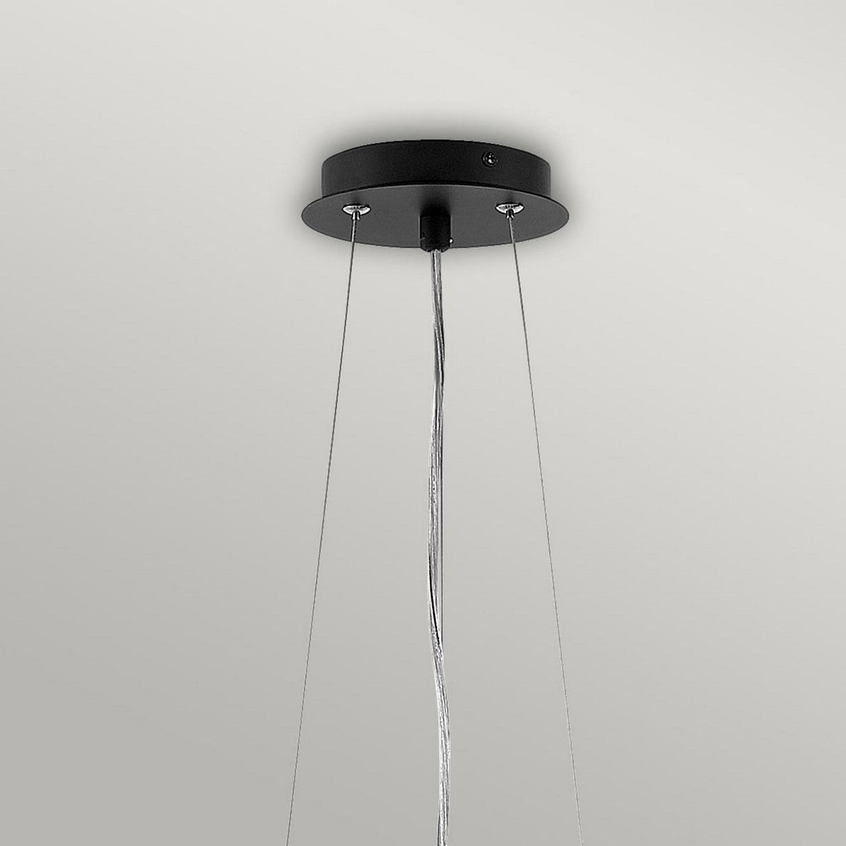 A modern ceiling light fixture in a contemporary design showcases a round black base and three thin suspension wires against a gray background. Mirroring the Zuma 6 Light Chandelier - Satin Black/Silver, these wires converge at the base, securely holding the geometric form in place.