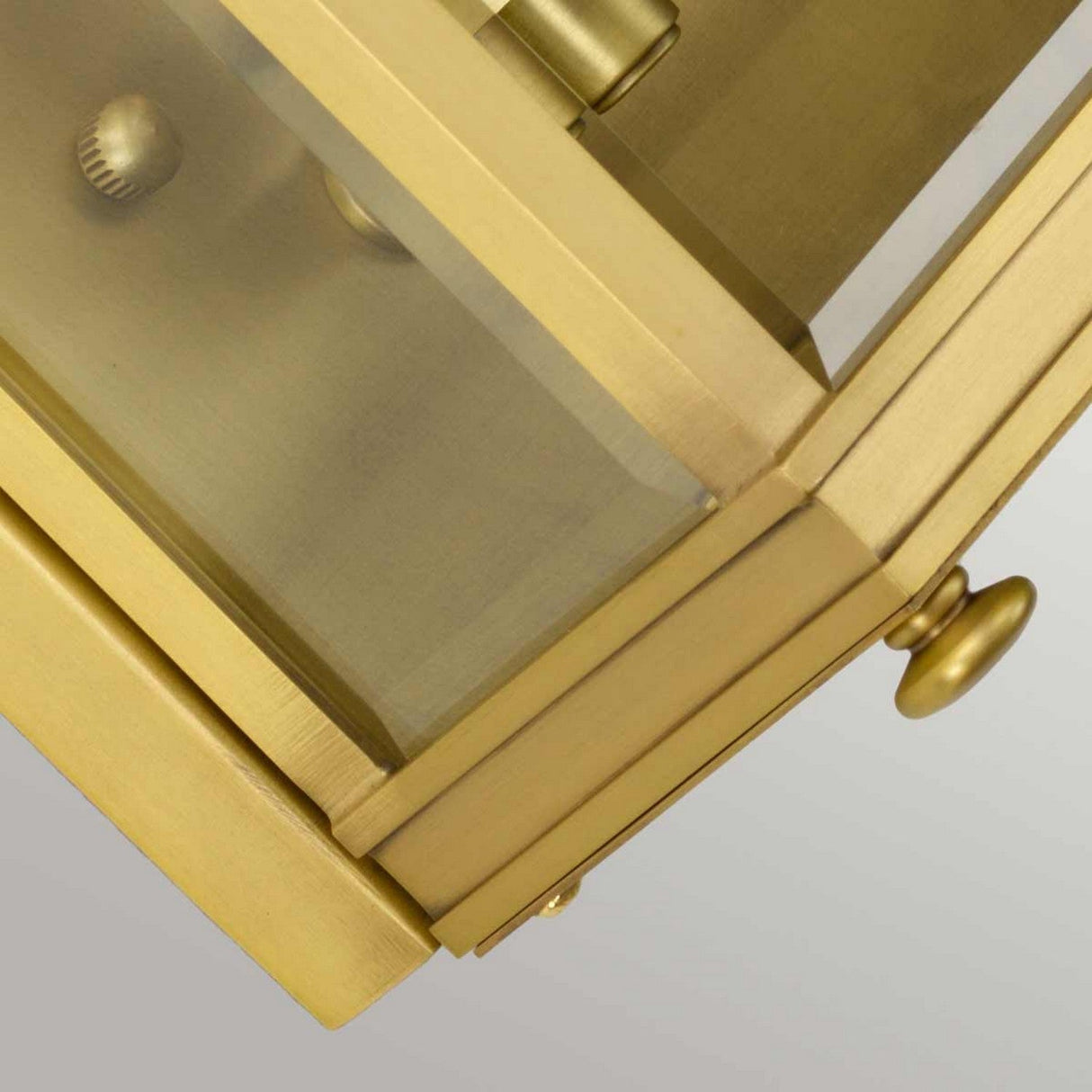 Close-up view of the Holborn 2 Light Outdoor Wall Light in brushed brass, showcasing a clear glass panel with visible hinges and knob. The metallic surface has a shiny, polished finish that evokes Georgian-inspired design against a light gray background.