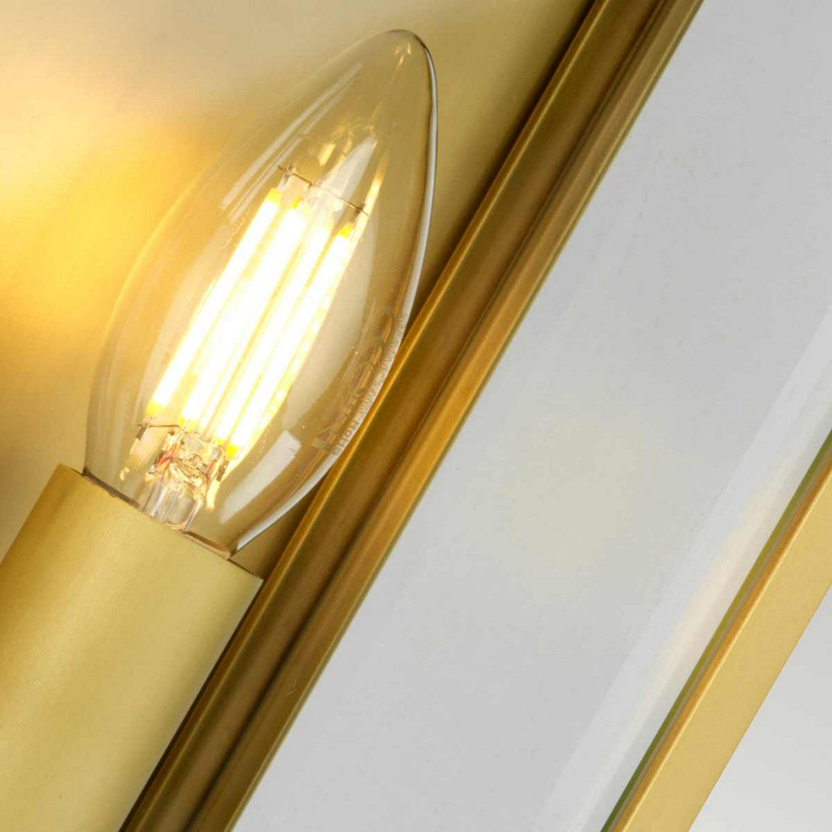 A close-up of the Holborn 2 Light Outdoor Wall Light - Brushed Brass, featuring an illuminated vintage-style LED bulb with a warm glow, mounted beside a mirrored surface, exuding a subtle Georgian-inspired design.