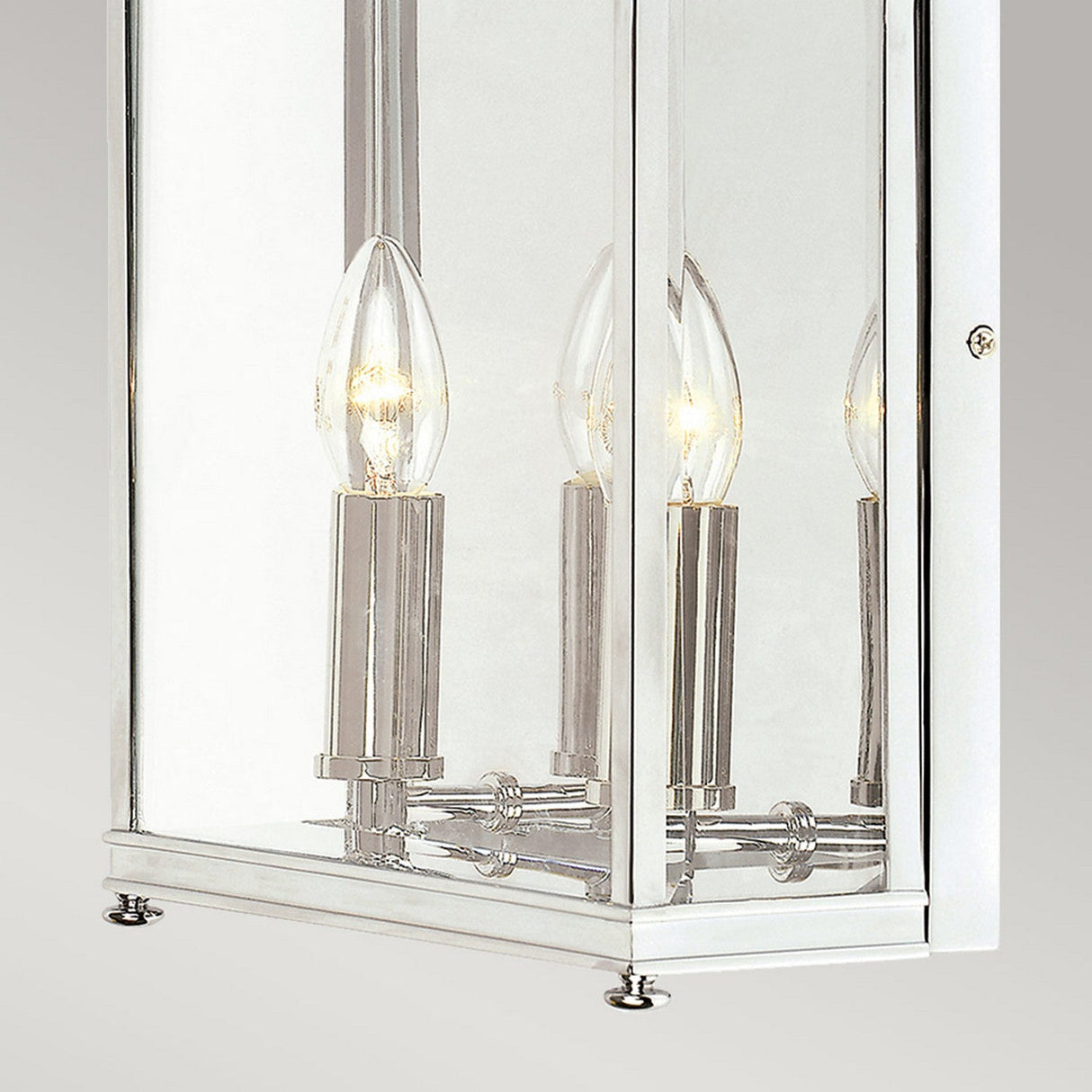 A close-up of the Holborn 2 Light Outdoor Wall Light in polished chrome, featuring a lantern-style design. It includes two candle-shaped bulbs enclosed in a clear glass casing. When illuminated, these bulbs emit a warm glow that enhances its elegant design, adding timeless charm against the plain gray background, reminiscent of Georgian elegance.