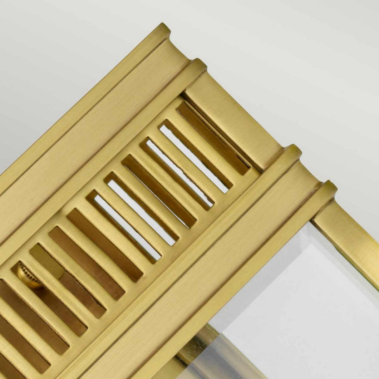 The Holborn 1 Light Outdoor Small Wall Lantern in brushed brass showcases a vent-like design with parallel slits, highlighting its gold-colored metal frame. The edges of the lantern exude Georgian elegance, with fine detailing and a partially visible transparent surface beneath the frame.