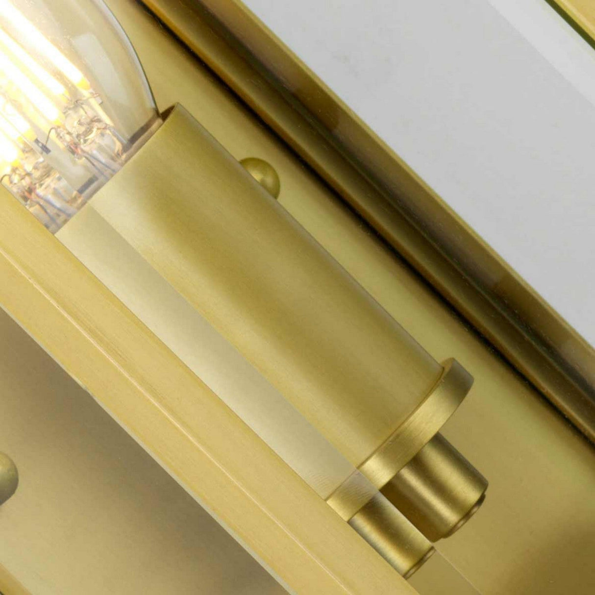 Close-up of the Holborn 1 Light Outdoor Small Wall Lantern in brushed brass, showcasing a visible bulb. The fixture features a smooth, cylindrical design with a reflective surface that exudes Georgian elegance and creates an elegant and sleek appearance.