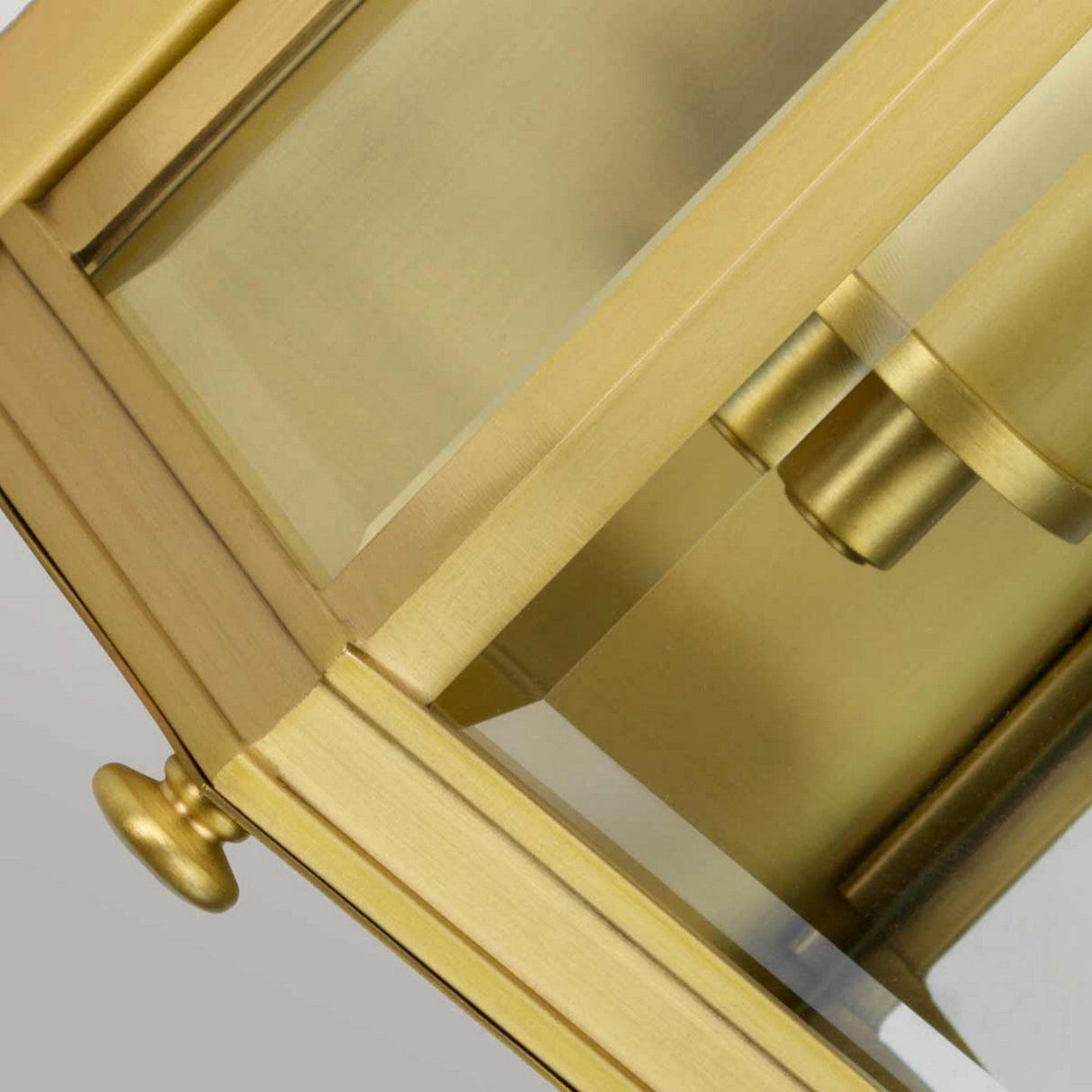 Close-up of the Holborn 1 Light Outdoor Small Wall Lantern, showcasing its modern geometric design with clear glass panels and sleek cylindrical elements. The brushed brass finish adds a sophisticated and stylish touch with a hint of Georgian elegance.