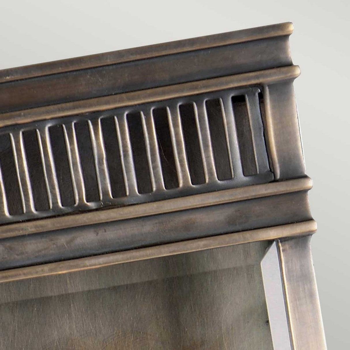 A close-up of the Holborn 1 Light Outdoor Small Wall Lantern in Dark Bronze showcases its decorative frame with a metallic finish. Reminiscent of Georgian lighting, the design features vertical grooves along the top section that add texture and detail. The angle highlights the craftsmanship and reflective surface of this elegant lantern.