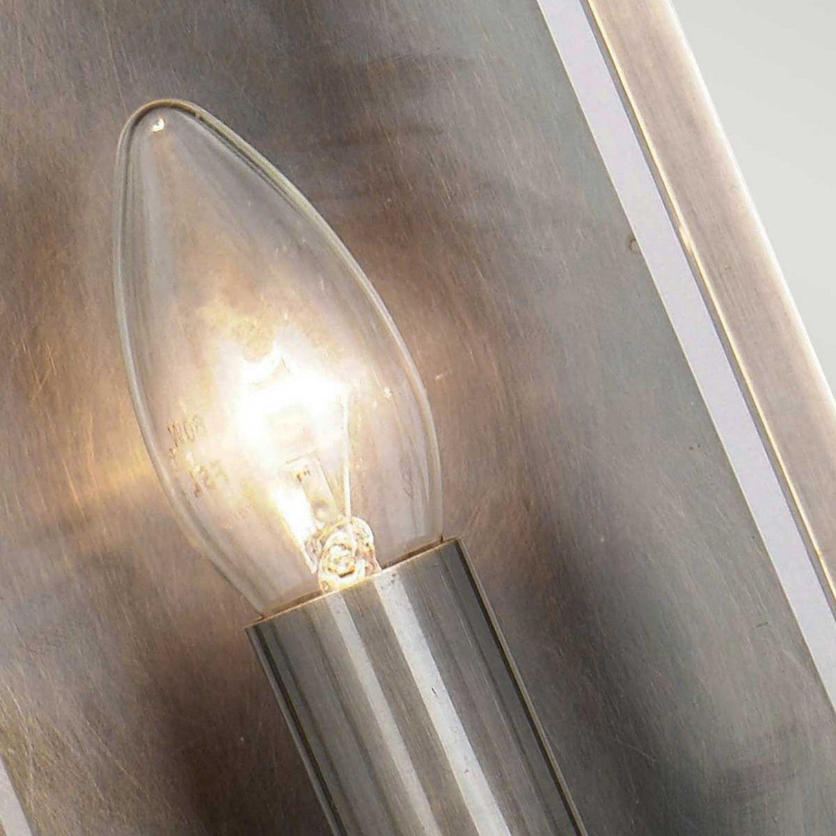 The Holborn 1 Light Outdoor Small Wall Lantern in dark bronze, featuring a candle-shaped design reminiscent of Georgian outdoor lighting, is mounted on a metallic fixture and placed on a reflective surface. The surrounding area is beautifully illuminated by the lantern's warm glow.