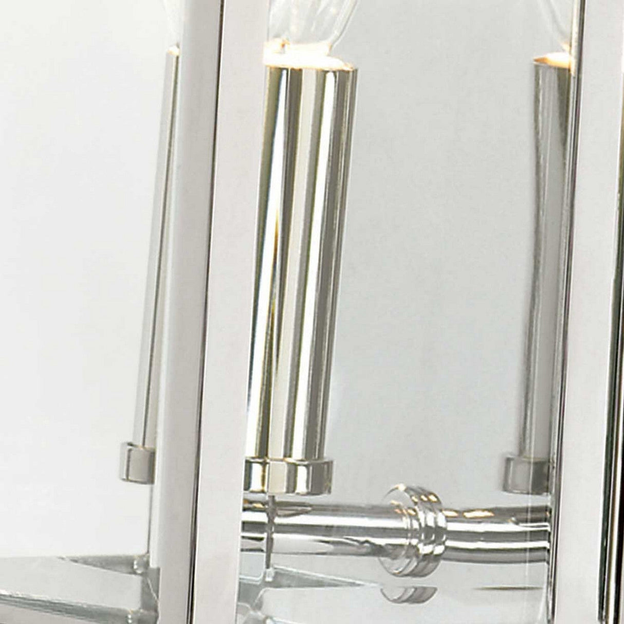A close-up of the Holborn 1 Light Outdoor Small Wall Lantern in polished chrome showcases its reflective glass panels, highlighting two partially visible light bulbs housed within sleek, modern cylindrical holders. The shiny surface beautifully captures elements of its surroundings, infusing any space with a touch of contemporary elegance.