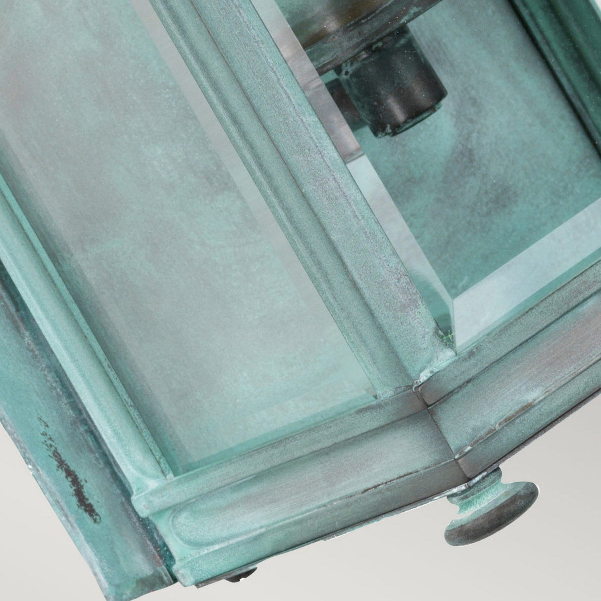 Close-up of the Holborn 1 Light Outdoor Small Wall Lantern in a verdigris finish, showcasing its glass panels and central metal fixture. This outdoor lighting piece has an aged look with visible screws and a textured surface.