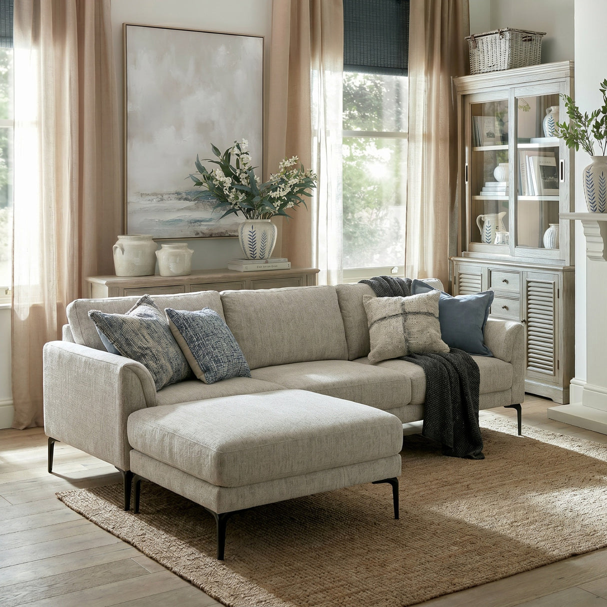 Hill Interiors Vaxeer three seater sofa with matching footstool in white upholstery on black metal legs, styled with blue cushions in a bright living room.
