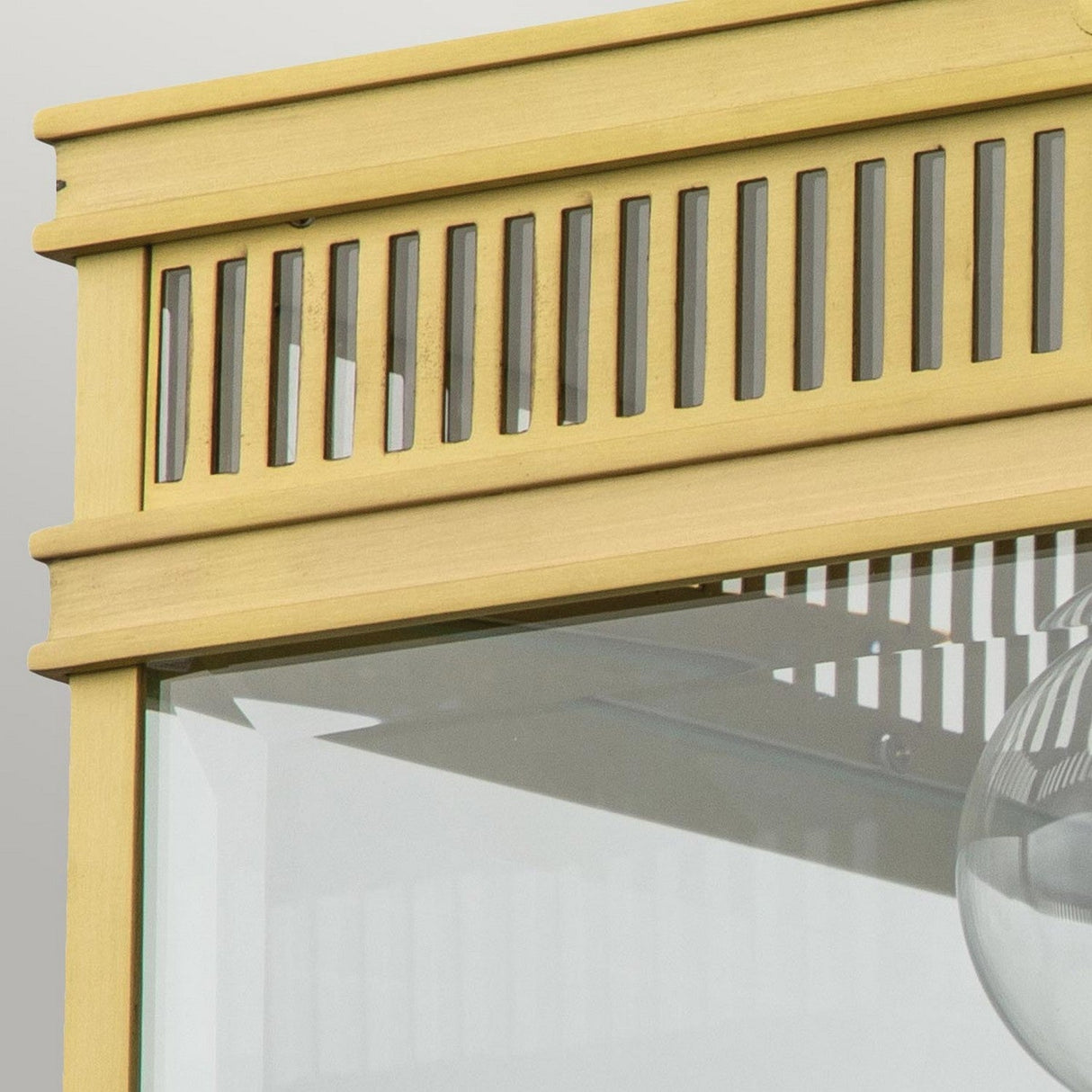 Close-up of a Holborn 2 Light Outdoor Flush in brushed brass, showcasing a decorative slatted design reminiscent of Georgian styles on the top edge. The finish has a light yellow tint, and part of a glass panel is visible below.