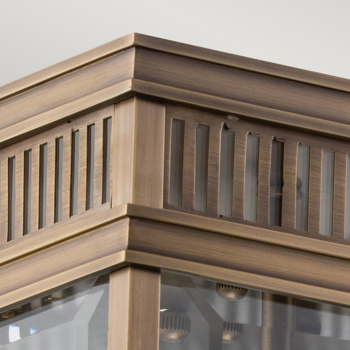 Close-up of the corner of the Holborn 2 Light Outdoor Flush, a decorative solid brass lantern with vertical slatted details and semi-transparent glass panels. This outdoor lighting piece features a warm, dark bronze finish that enhances its vintage aesthetic.