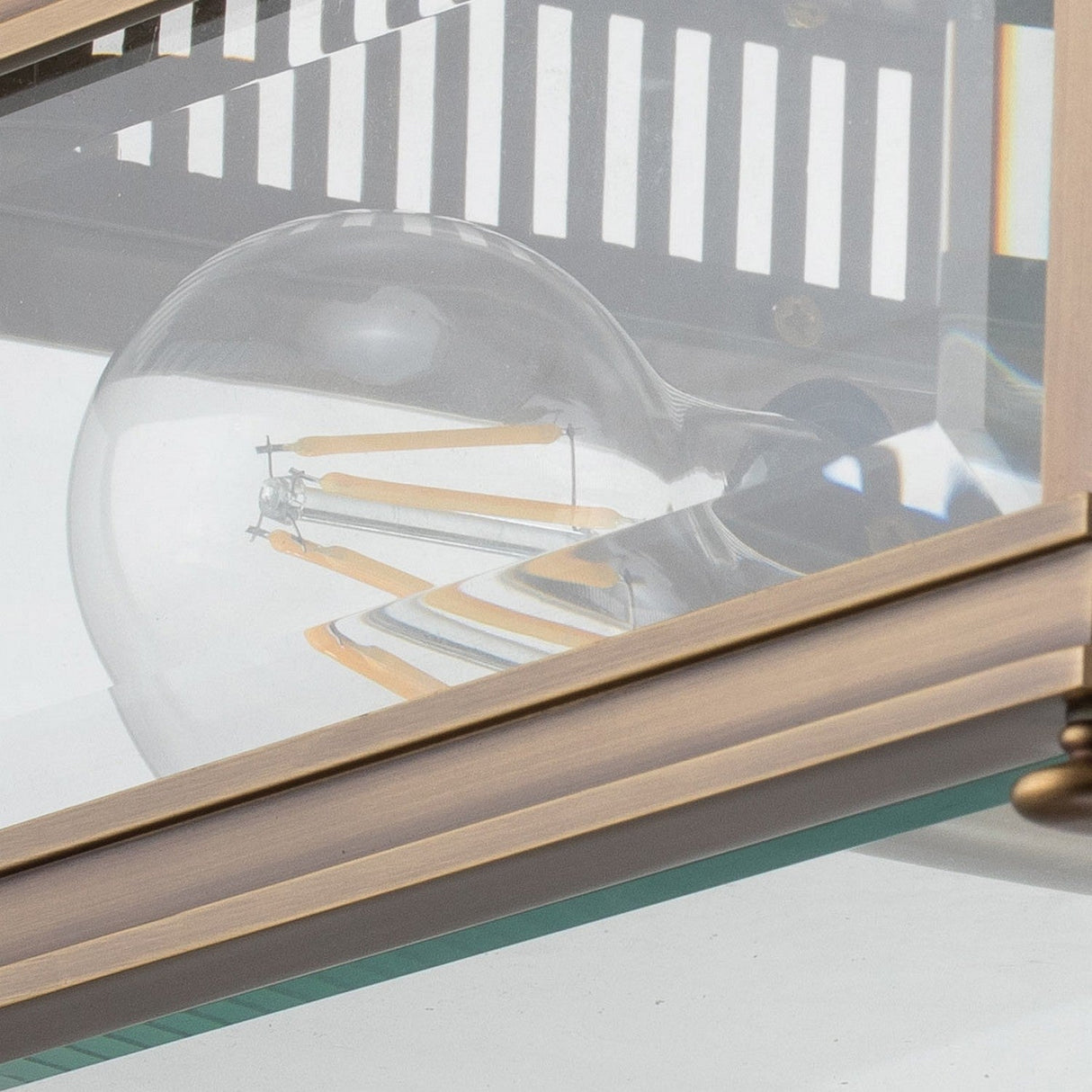 Close-up of a decorative light bulb inside the Holborn 2 Light Outdoor Flush - Dark Bronze, showcasing visible LED filaments and reflections on the glass panels within its solid brass and glass lantern fixture.