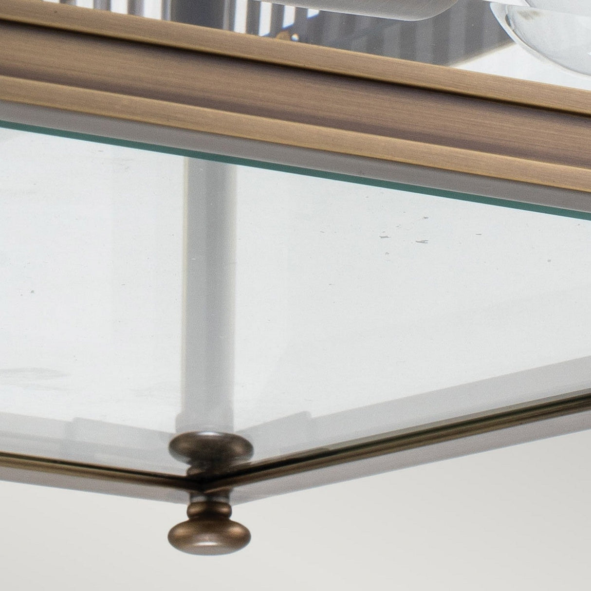 A close-up of the Holborn 2 Light Outdoor Flush in dark bronze reveals its solid brass frame, showcasing a sophisticated modern design with clean lines and a reflective surface. The softly blurred background highlights the metallic and glass textures of the piece.
