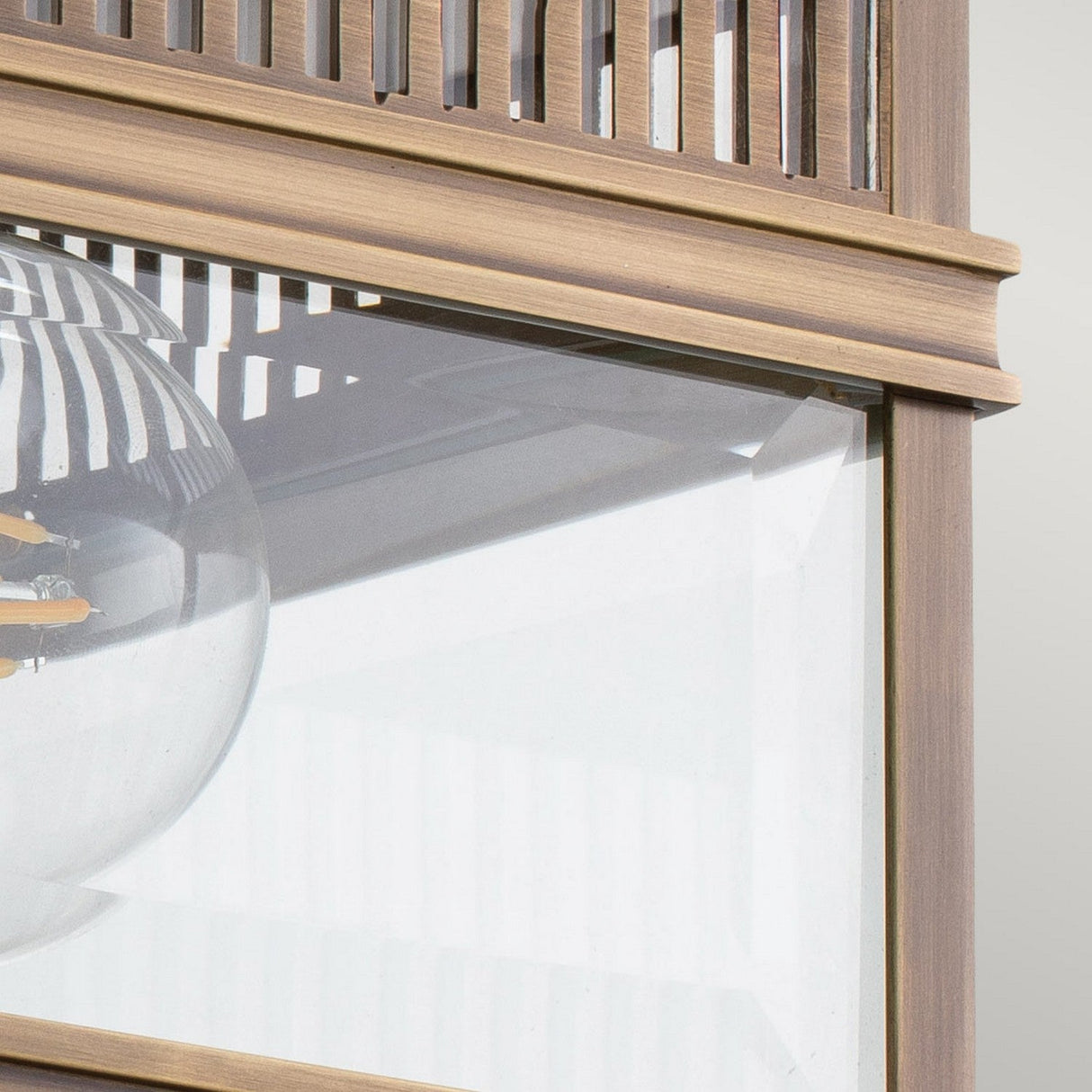 Close-up of a dark bronze Holborn 2 Light Outdoor Flush with vertical slats and a clear glass panel. Behind the glass, part of a round, transparent light bulb with visible filaments is seen. The fixture, combining traditional allure with modern design elements, is perfect for outdoor lighting.