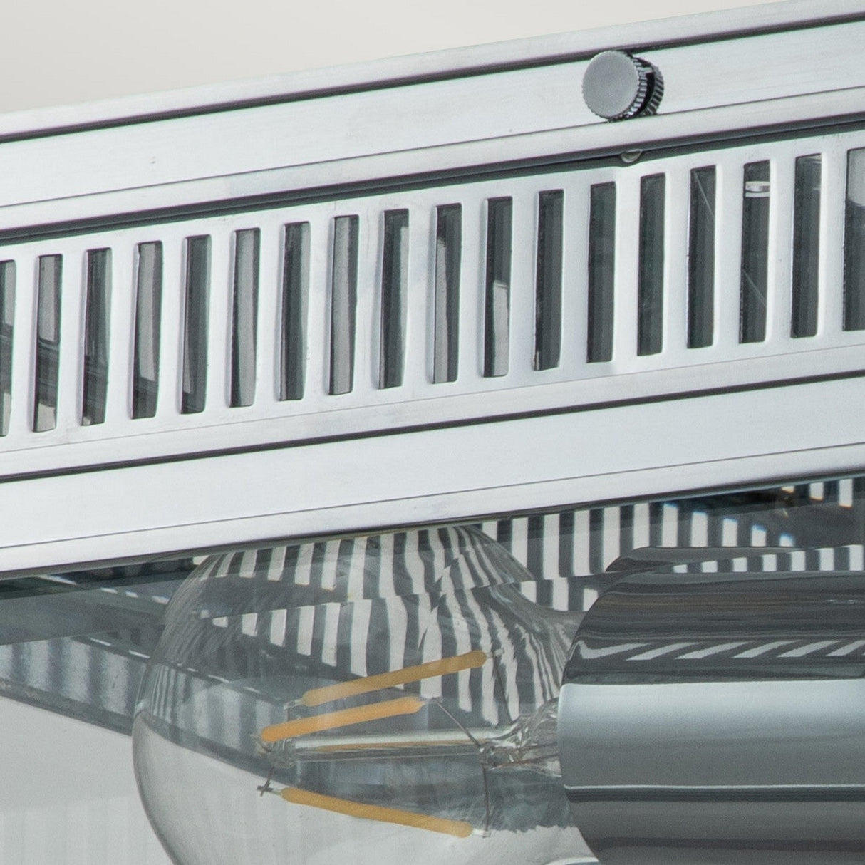 Close-up of the Holborn 2 Light Outdoor Flush in polished chrome, showcasing a modern metal light fixture with visible LED bulbs featuring yellow filaments encased in clear glass. It boasts sleek horizontal and vertical slats, making it ideal for outdoor lighting with its IP44 rating.