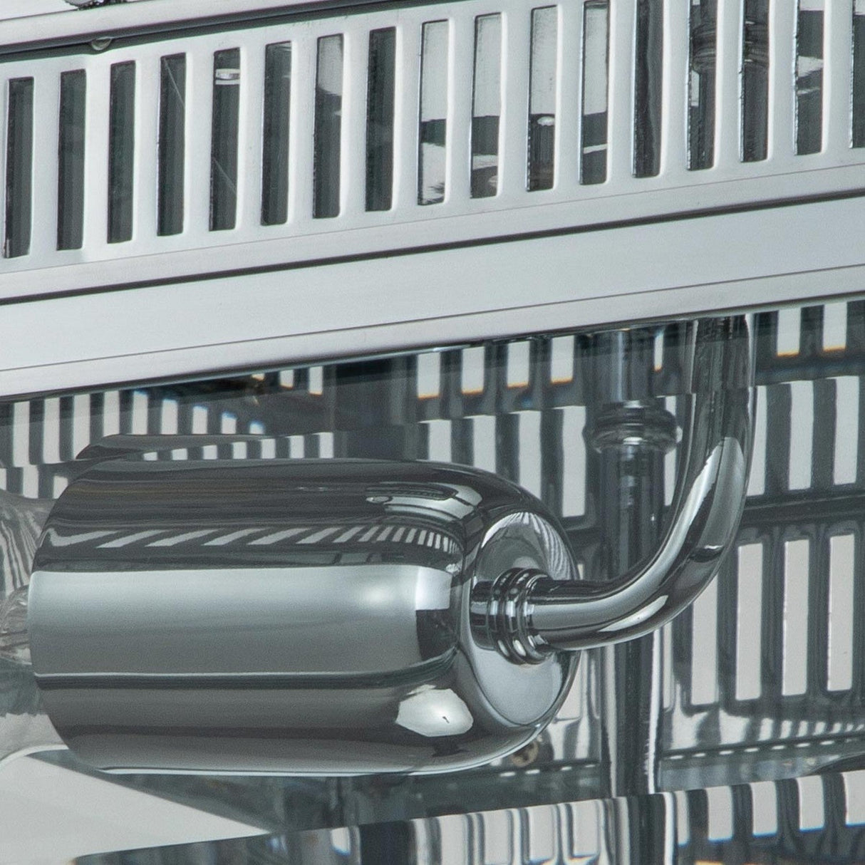 Close-up of the Holborn 2 Light Outdoor Flush in polished chrome, featuring its sleek metal surface with a cylindrical steam wand attachment. The image accentuates the product's reflective finish and stainless steel elements, evoking outdoor lighting aesthetics. Rows of vertical slits adorn the upper part of this espresso machine-inspired design.