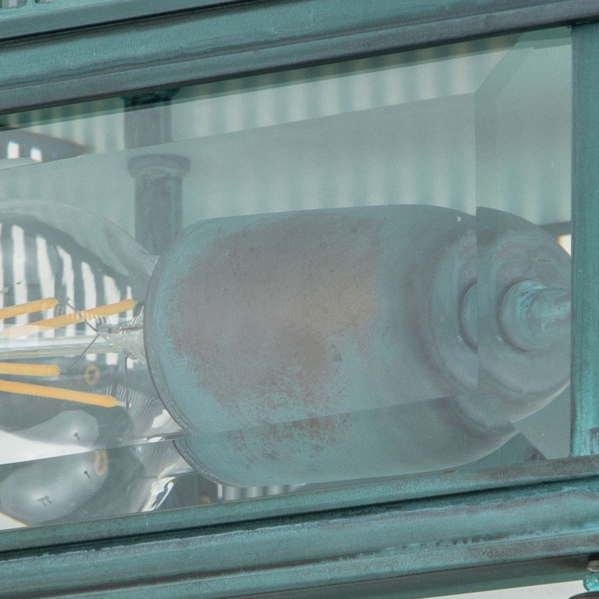 Close-up of the Holborn 2 Light Outdoor Flush - Verdigris, featuring a vintage-inspired light bulb encased in a glass lantern with a verdigris finish. The internal filaments and cylindrical shape are clearly visible, along with the reflective glass surface.
