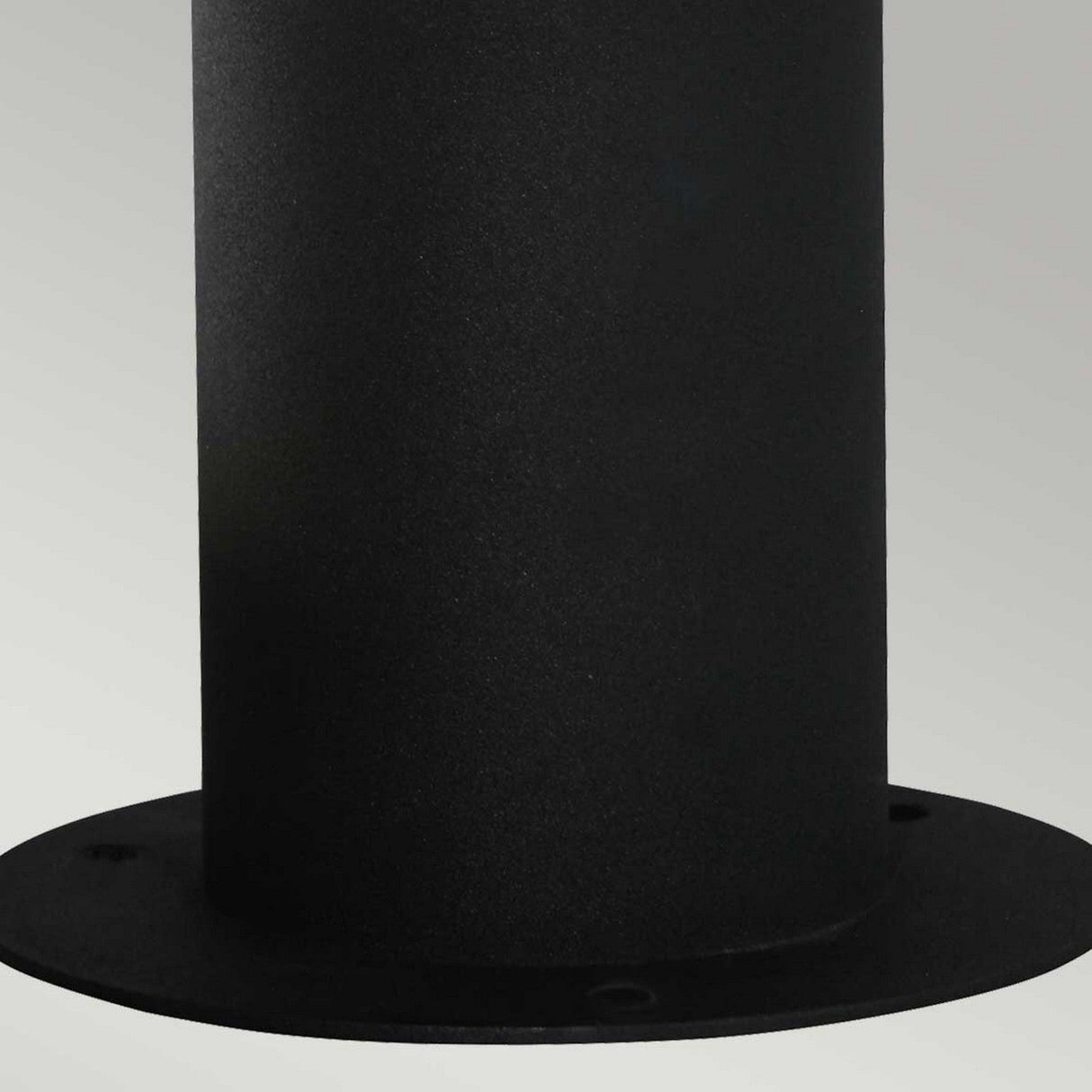 The Hornbaek 1 Light Pedestal Light in black is showcased up close, revealing its cylindrical shape with a flat base featuring several small holes, set against a plain light gray background. Its smooth matte surface and minimalist style evoke Scandinavian design, reminiscent of an elegant outdoor fixture.