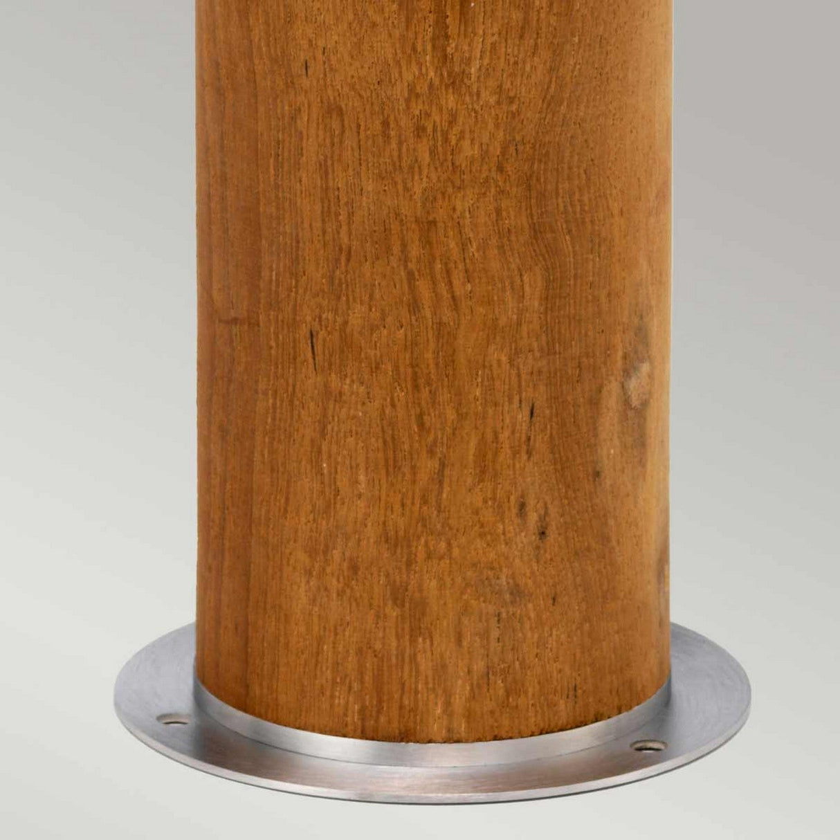 A close-up of the Hornsea 1 Light Bollard in brown, featuring a teak wood cylindrical pole with a smooth, natural finish, mounted on a sleek stainless steel base. The background is simple and neutral gray.