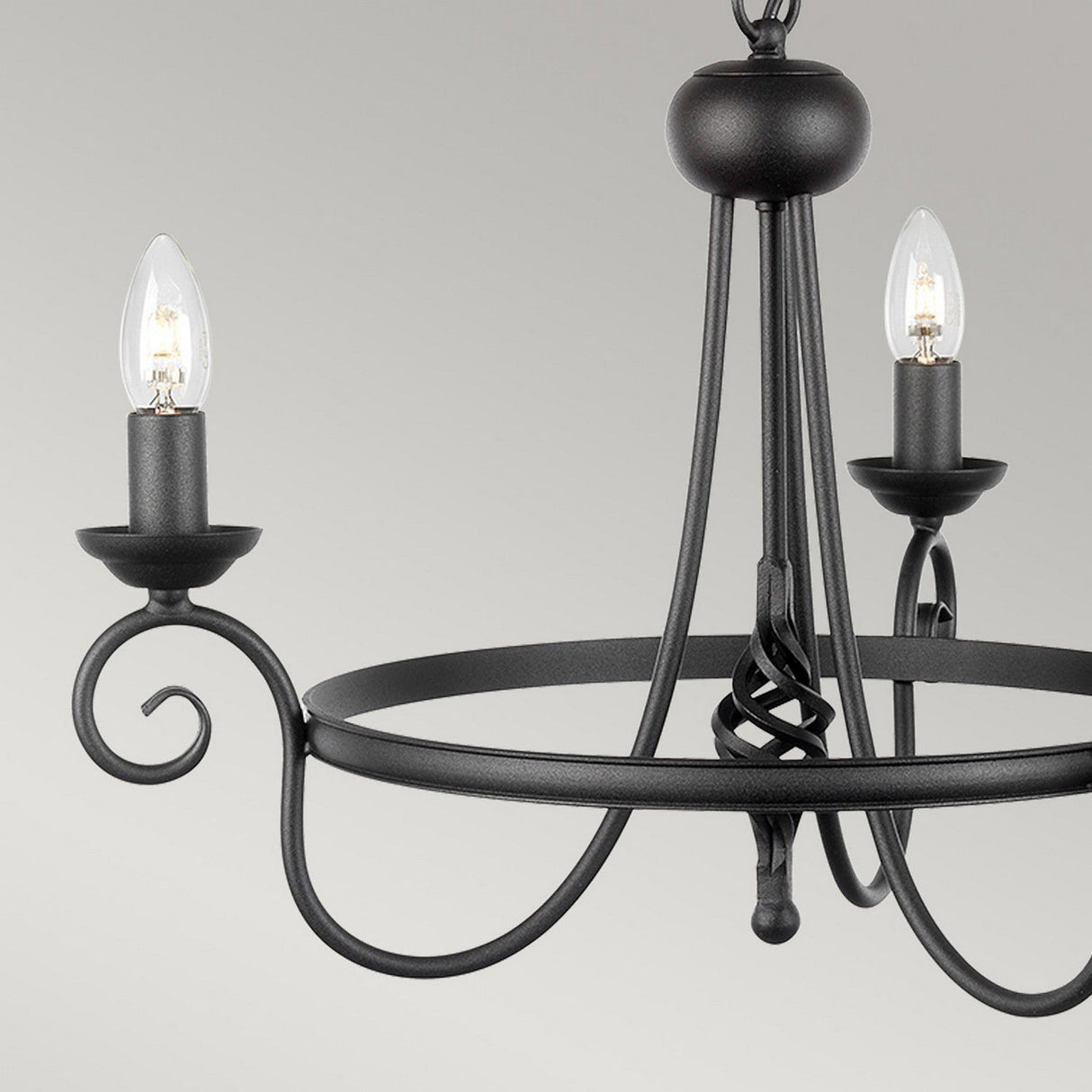 The Harlech 3 Light Chandelier - Black, designed with medieval elements, displays a black metal frame with graceful scrollwork arms and three candle-style lights, providing a classic accent against a gray background.
