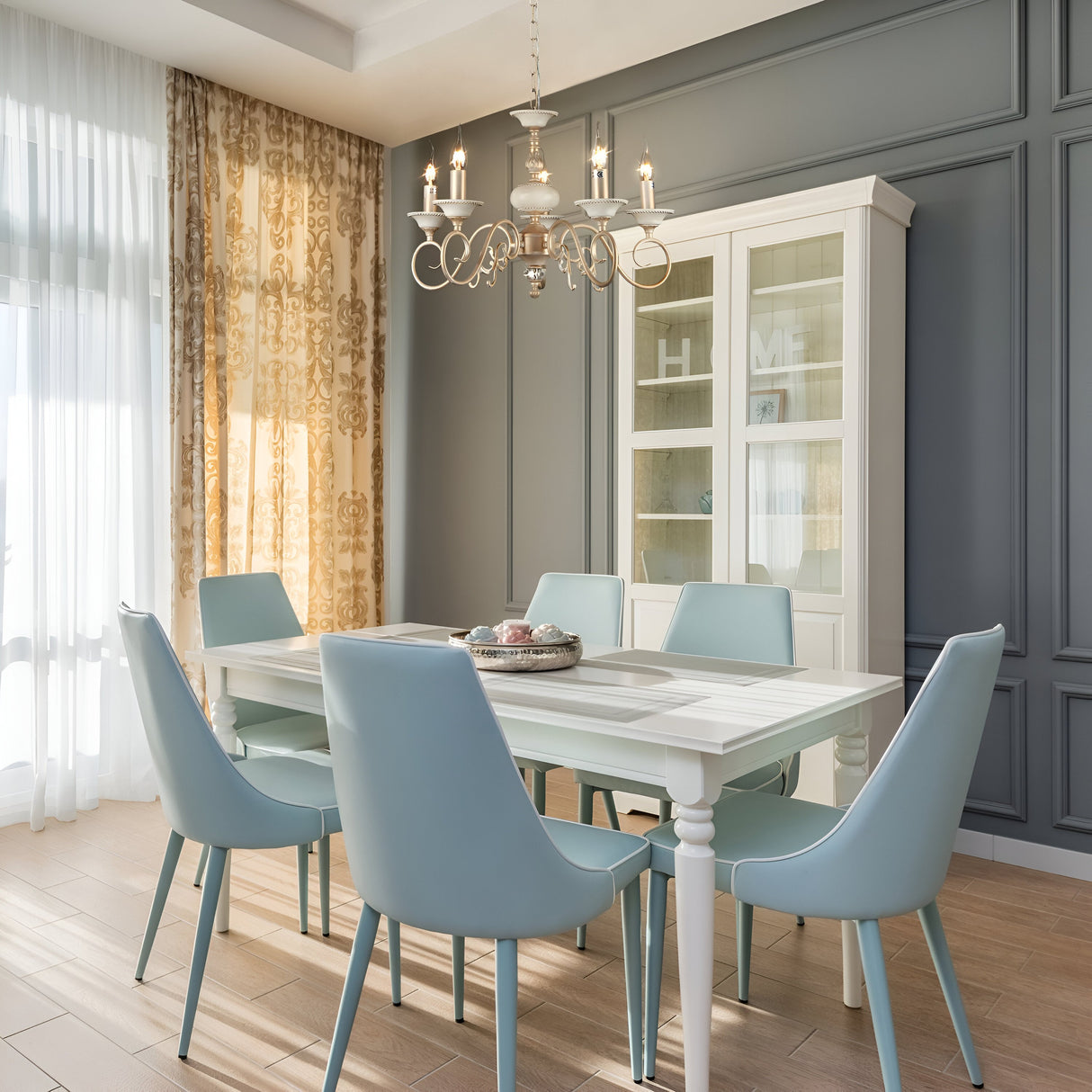 The dining room showcases an elegant design with a white table, six light blue chairs, and the luxurious Perla 5 Light Chandelier in gold and cream overhead. It features a glass cabinet, dark panel wall, light wood flooring, and floral-patterned curtains on large windows.