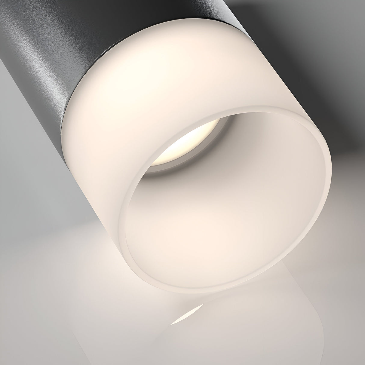 Close-up of a Pauline Long Round Surface Downlight - Black, showcasing its modern cylindrical design and ambient lighting. Its sleek finish embodies modern minimalism as it mounts on a white ceiling, casting a gentle glow below.