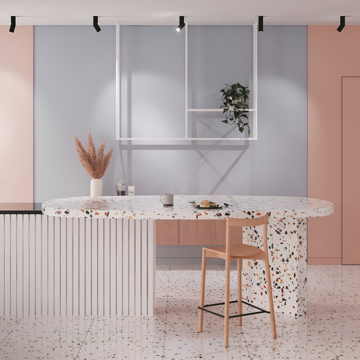 A modern kitchen with a terrazzo island of multicolored speckles and a wooden bar stool, enhanced by the Dafne LED Single Spotlight 10W 3000K in Black. Pampas grass in a vase and a pastry cup adorn the minimalist pastel backdrop, while a grid frame with a plant is on the wall.
