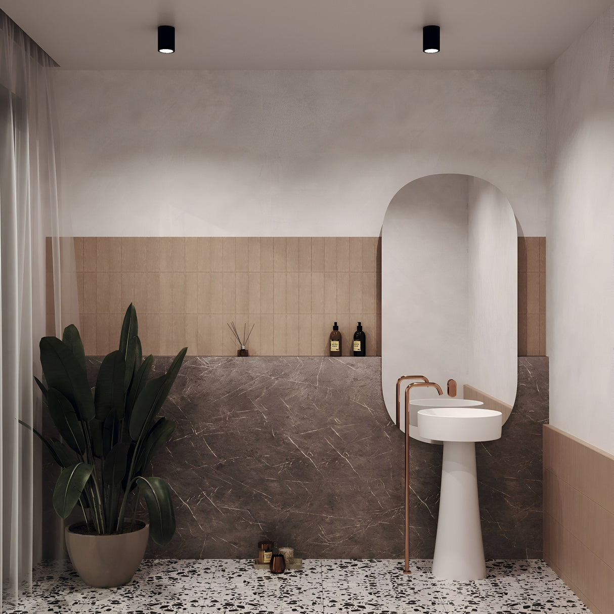 A minimalist bathroom showcases a large oval mirror above a modern pedestal sink with a copper faucet. A potted plant is illuminated by the Zoom Round Surface Downlight in black on the left, as shelves display toiletries and a terrazzo-patterned floor complements beige tiles and dark stone walls.
