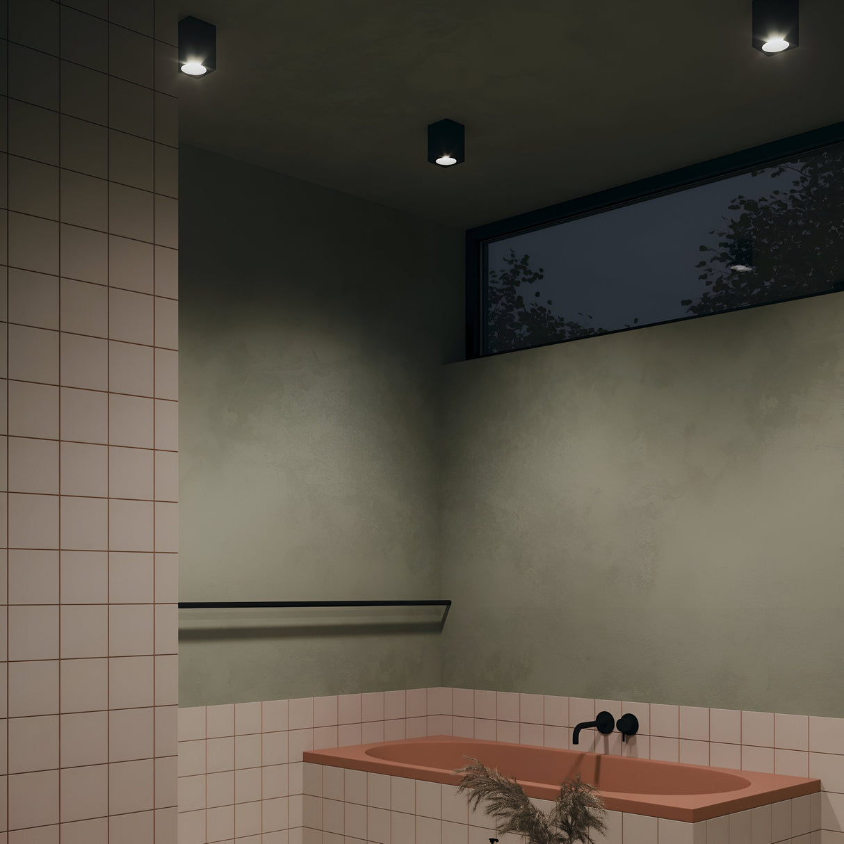 The minimalist bathroom features a greenish-gray wall and ceiling with recessed Zoom Square Surface Downlights in black, boasting an IP65 rating. A horizontal window, coral bathtub with matte black faucet, white tiled walls, black towel bar, and pampas grass adorn the space elegantly.