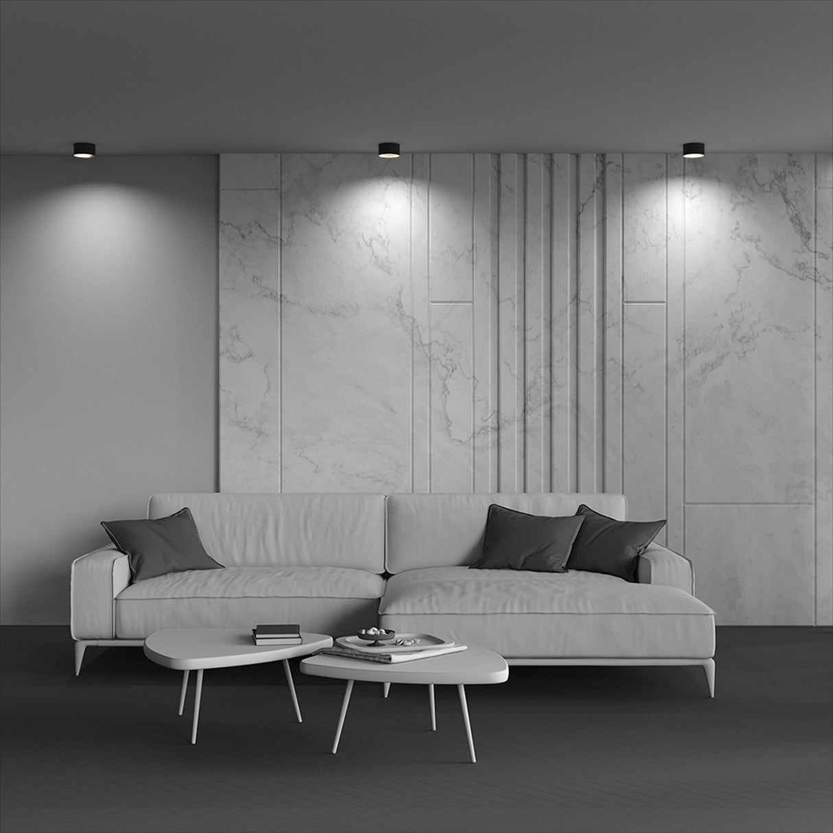 A modern living room showcases a minimalist design with a large white sectional sofa adorned with dark cushions. In front, two sleek coffee tables hold a book and bowl, while the Vega LED Round Surface Downlight 12W 3000K - Black enhances the marble-textured wall behind, adding depth to the interior style.