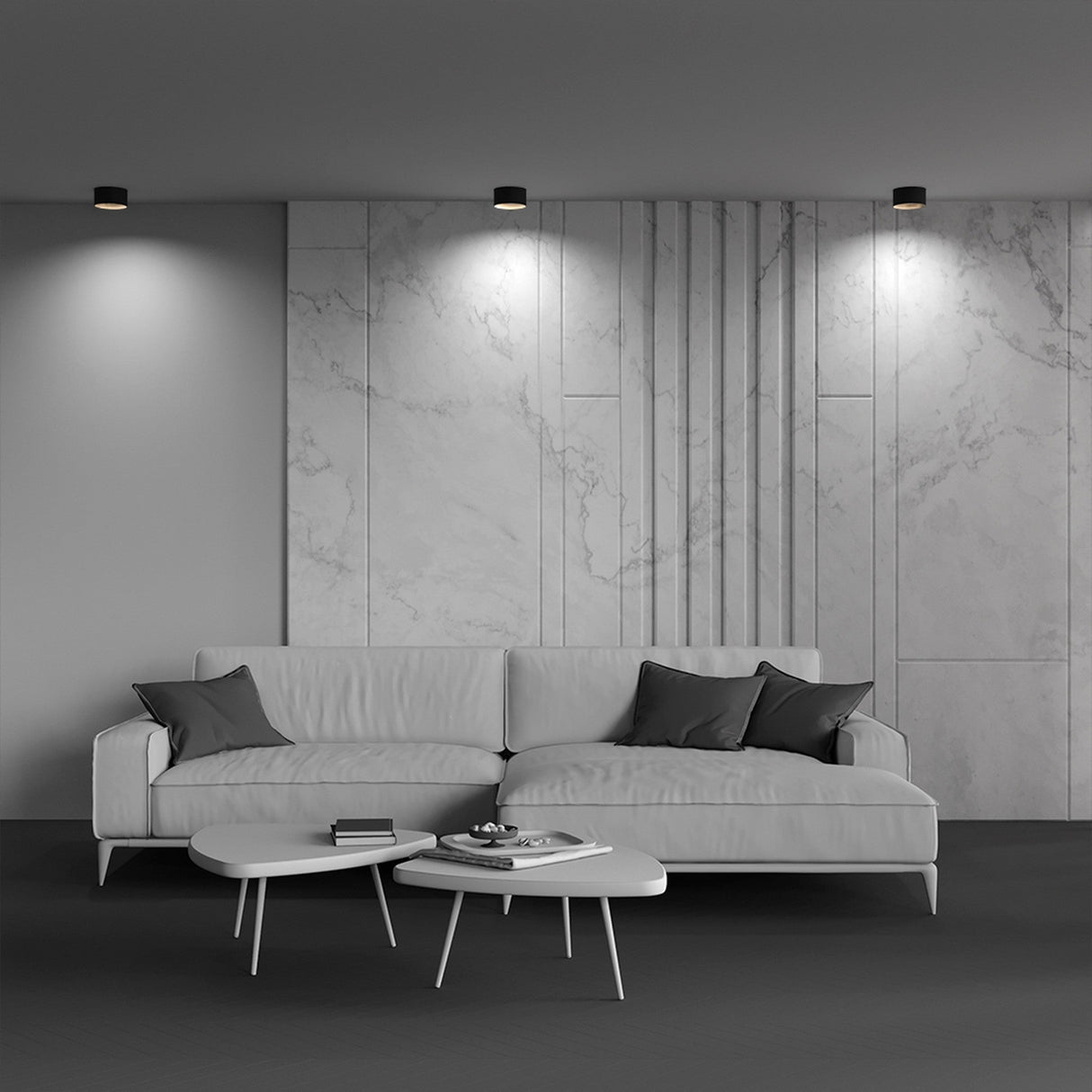 A modern living room features a gray couch with black cushions and a minimalist white coffee table on a dark floor. Marble wall panels are illuminated by Vega LED Round Surface Downlights 15W 3000K in Black & Matte Gold. A book and decorative item adorn the table.