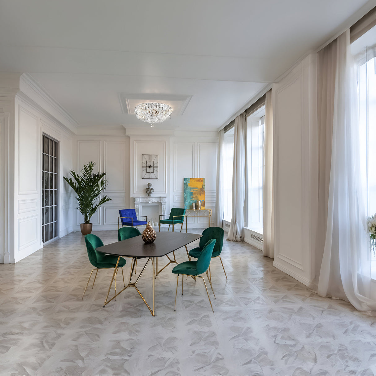 An elegant dining room features a dark oval table and green chairs on patterned marble flooring. Large windows with sheer curtains line the wall, while a Basfor 3 Light Crystal Chandelier - Nickel, adorned with diamond-cut crystals, hangs from the ceiling. A potted plant and artwork add decor.