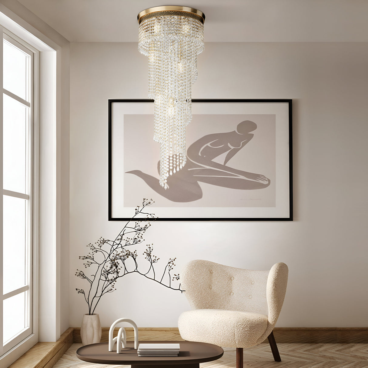 A stylish room features a modern chair and round table by the window, with opulent lighting. A large abstract art piece adorns the wall, while the Cascade 12 Light Crystal Chandelier in gold exudes elegance. A decorative branch in a vase on the table perfects the minimalist decor.