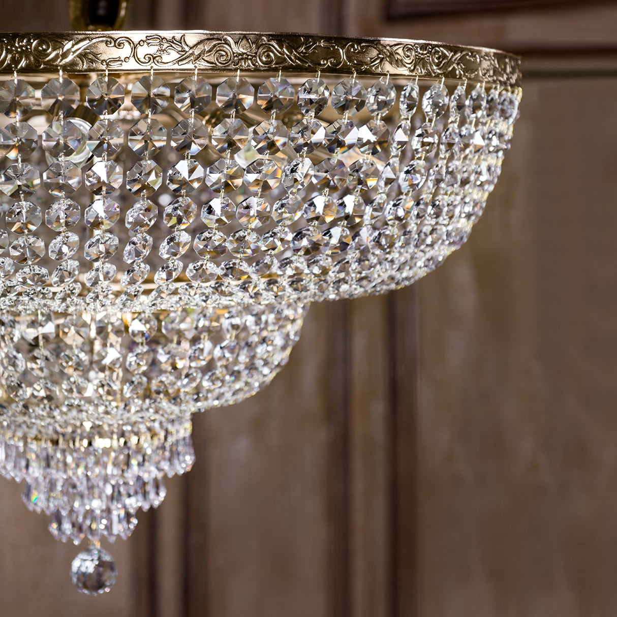 A close-up of the Palace 18 Light Crystal Chandelier - Gold showcases its cascading crystal pendants and ornate brass rim against a softly lit wooden or textured background, enhancing its luxurious lighting appeal.