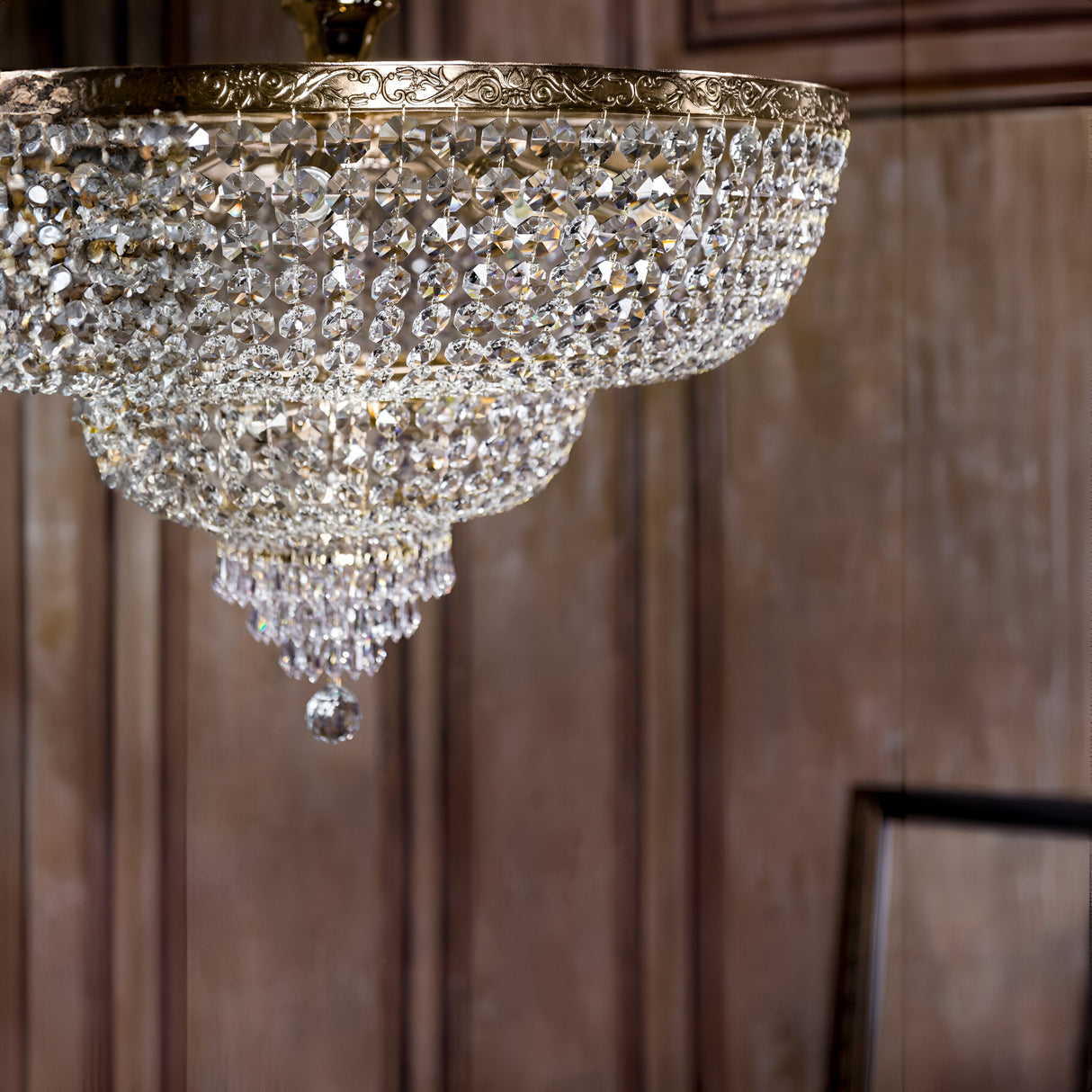 The elegant room is illuminated by the Palace 14 Light Crystal Chandelier - Gold, its shimmering crystal pendants forming a graceful bowl shape and crowned with a central hanging accent, perfectly complementing the wooden paneled walls.