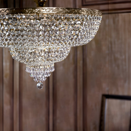 The elegant room is illuminated by the Palace 14 Light Crystal Chandelier - Gold, its shimmering crystal pendants forming a graceful bowl shape and crowned with a central hanging accent, perfectly complementing the wooden paneled walls.