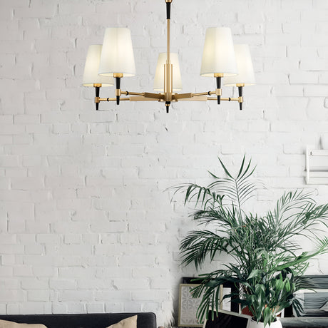 A white brick wall is adorned with a Zaragoza 5 Light Chandelier - Brass featuring five white lampshades above a black sofa, accompanied by a large green potted plant for a touch of nature in the minimalist room.