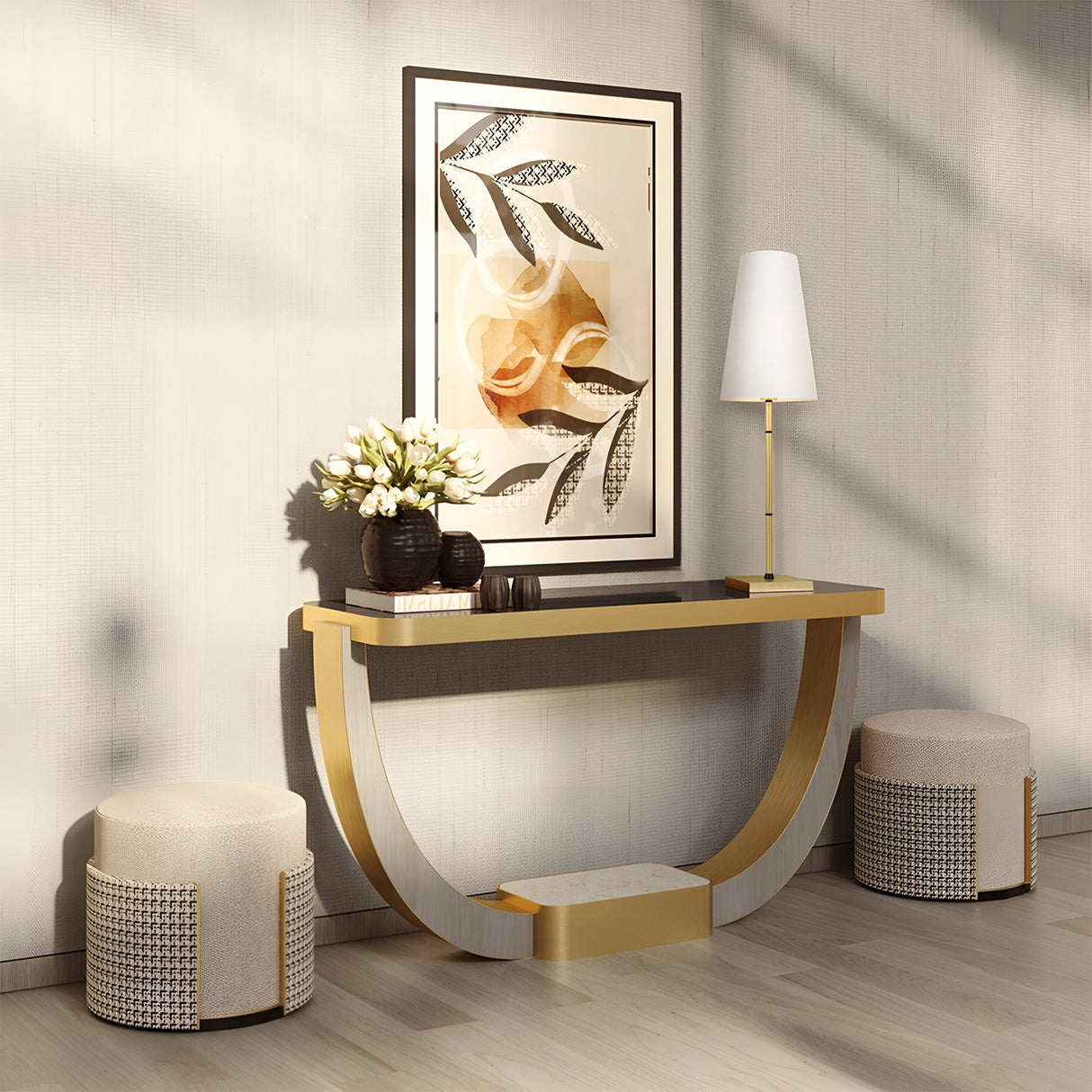 A modern room has a U-shaped console table with a brass finish displaying a floral bouquet, books, and the Zaragoza Table Lamp - Brass With White Fabric Shade. Above is leaf and rose artwork. Two textured stools sit below the table, enhanced by ambient lighting for coziness.