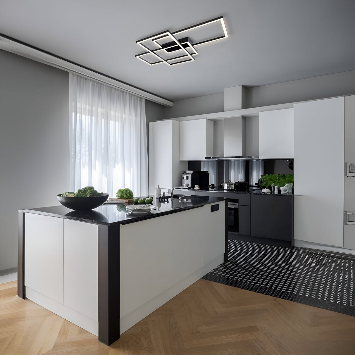 A modern kitchen features white cabinets and a black island countertop. Illuminated by the Line LED Ceiling Light - Black, the space is enhanced by stainless steel appliances. A patterned black and white rug contrasts with natural light through sheer curtains, casting a glow on green plants.