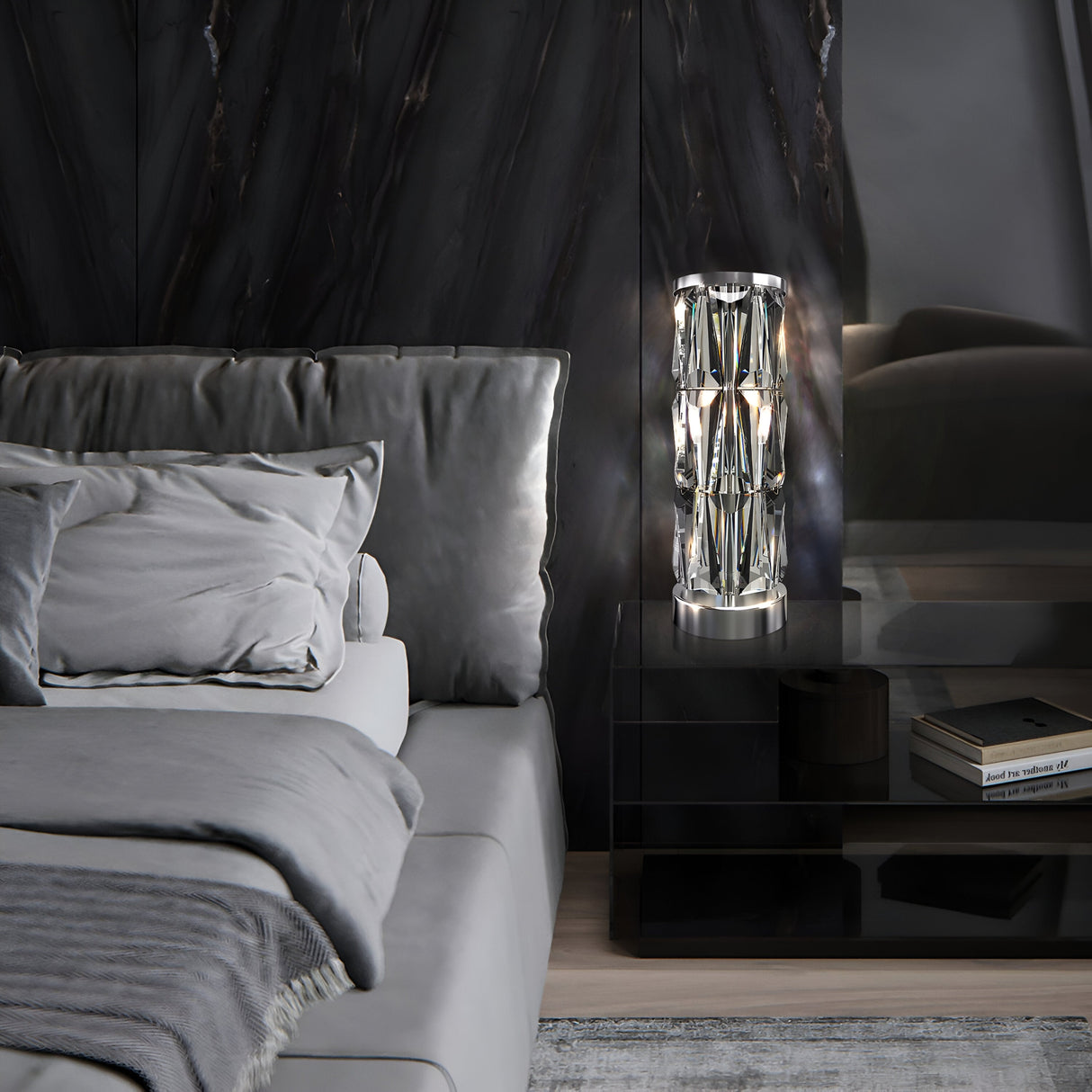 A modern bedroom boasts a light gray bed with a plush headboard and neatly arranged pillows. On a sleek black nightstand sits the Puntes Table Lamp in chrome, enhanced with crystal accents. The dark marbled wall adds elegance, complemented by a soft gray rug.