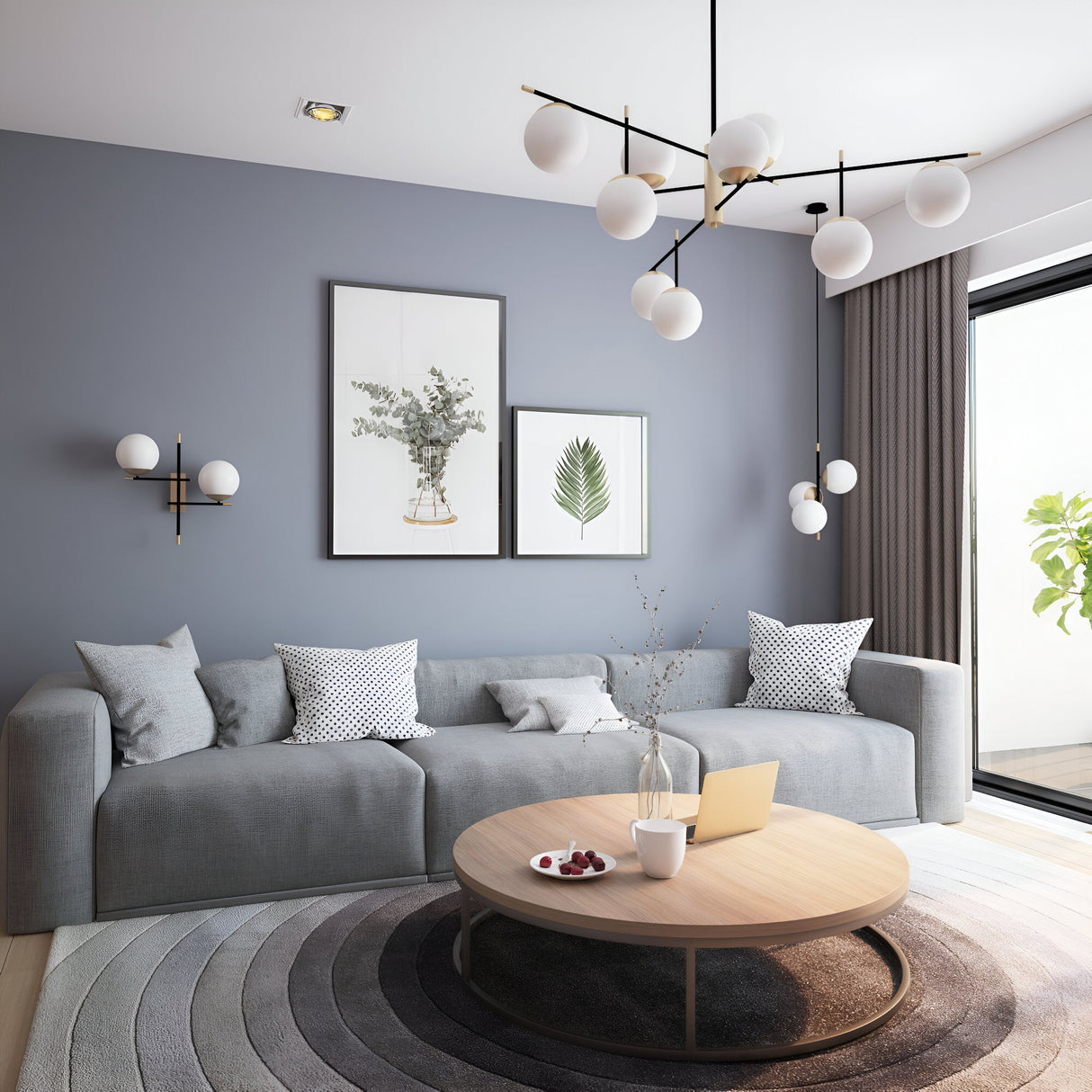 A modern living room features a gray sofa with decorative pillows, a wooden coffee table showcasing a laptop and fruit bowl. Abstract wall art complements the Nostalgia 9 Light Chandelier in gold, elegantly lighting the space. A large window reveals greenery, while a round rug enhances the floor.