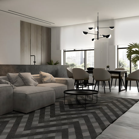 A modern living and dining area features a large gray sectional sofa, round coffee table, and geometric rug. Sleek dining chairs surround the table. The Mollis 8 Light Chandelier - Black hangs overhead, while big windows highlight a potted plant with an industrial design touch.