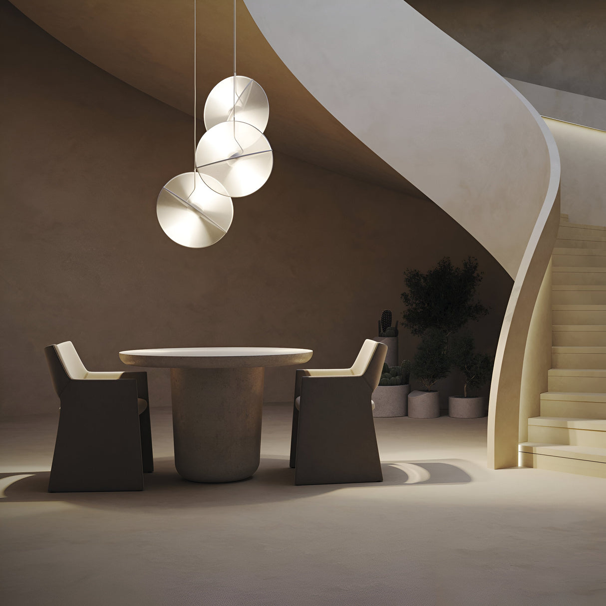 A modern, minimalist room with a round table and two angular chairs features ambient illumination from three orb-shaped lights. The Reflex 3 Light LED Disc Pendant - White enhances the glow. A curved staircase ascends, with potted plants against smooth beige walls.