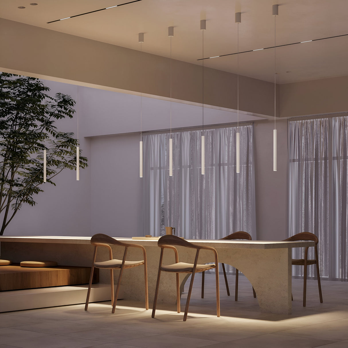 A modern dining area features a minimalist design with a sleek table and three wooden chairs. The Pro Base LED Thin Pendant Light in white stylishly hangs above, casting a gentle glow. Soft natural light filters through sheer curtains, while a tall plant adds greenery to the serene space.