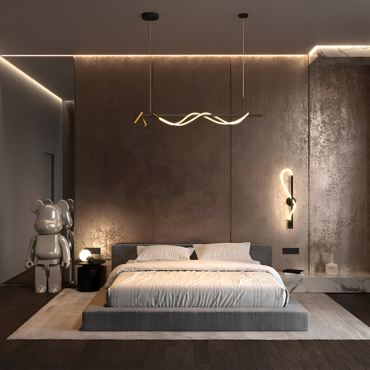 A modern bedroom showcases a large low-platform bed with gray bedding. The walls have a metallic finish, and contemporary lighting includes a sculptural fixture above the bed. On the left, theres a decorative bear sculpture and a small round table featuring the Tau LED Linear Suspension Light 3000K 30W - Black With Gold. Warm lighting enhances the ambiance.