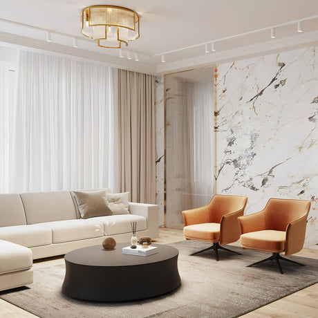 A modern living room features a beige sofa, two orange armchairs, a round black coffee table, and a large marble-patterned wall. Sheer white curtains adorn the windows, while the Frame 9 Light Flush - Gold fixture with embossed glass tubes elegantly hangs from the ceiling.